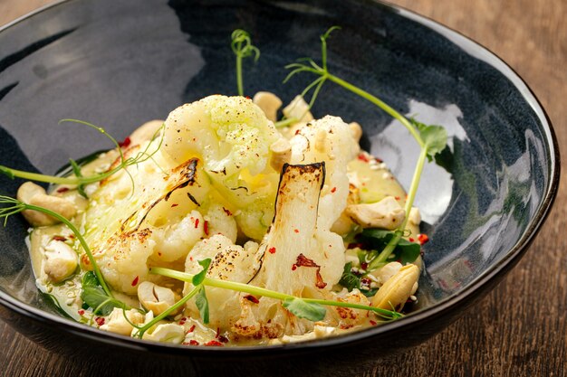 Close up on cauliflower with tofu sauce and cashews in a black bowl