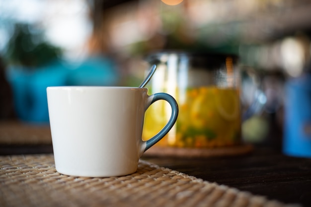 Close-up ceramic Cup on wooden table on glass teapot background with herbal tea, sea buckthorn and mint