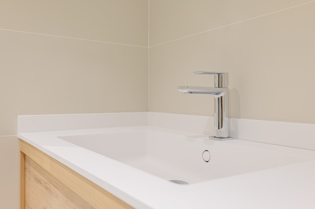 Close-up of ceramic washbasin on wooden vanity cabinet with modern metal faucet in bathroom.