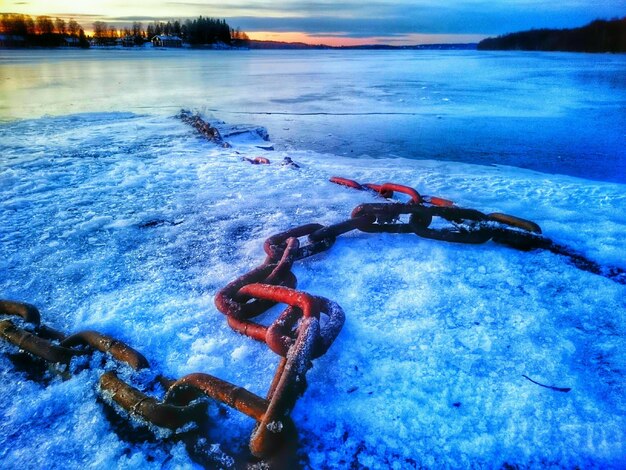 Close-up of chain on snow covered riverbank during sunset