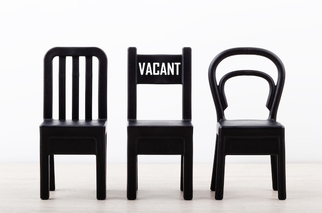 Close-up of a chair with text Vacancy among black chairs in a row