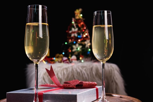 Close-up of champagne flutes by christmas decoration on table against black background