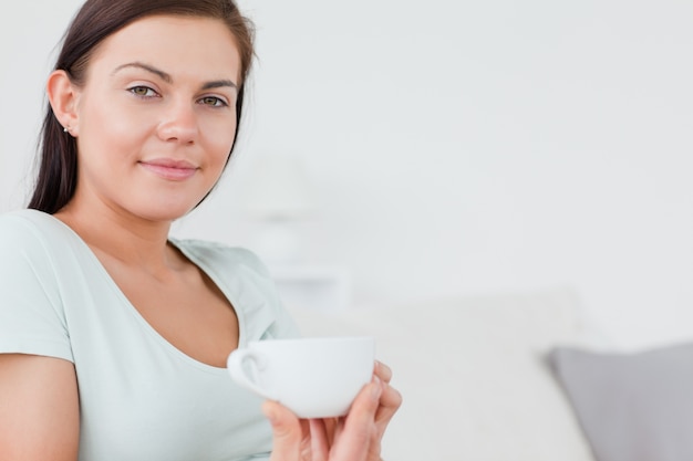 Close up of a charming woman sitting on a sofa with a cup of tea