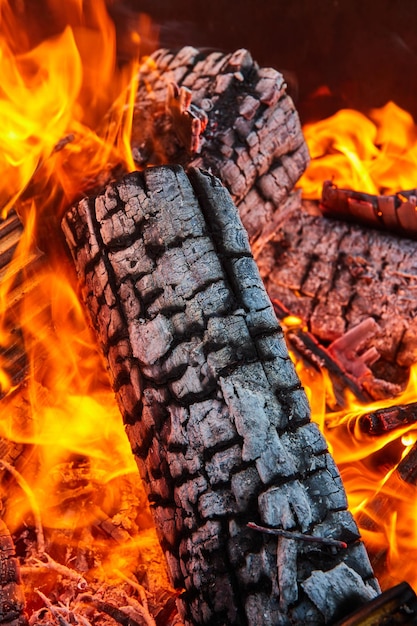 Close up of charred black log with white ash coating surrounded by orange flames background asset