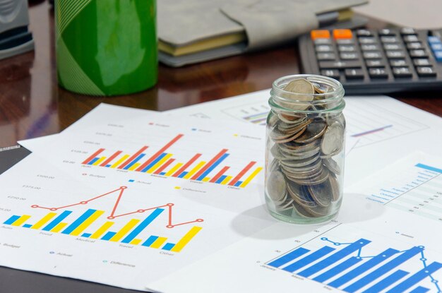 Close-up of chart papers with coins in jar on desk