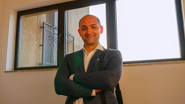 Close up of cheerful boss looking at camera and smiling standing on stairs in corporate building. Good looking successful businessman, team leader in modern company office.