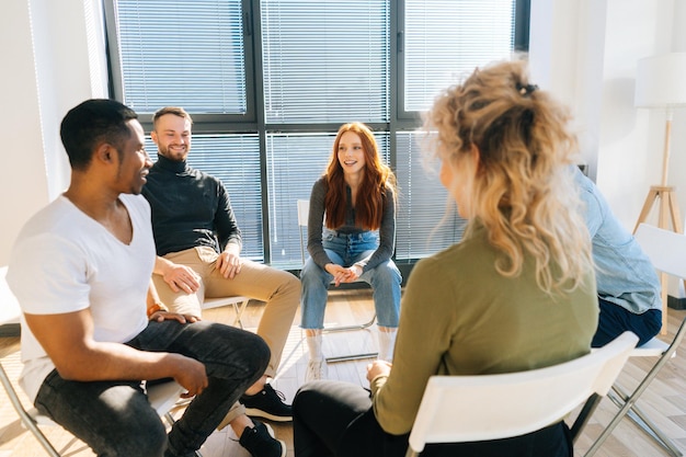 Close-up of cheerful coworkers sitting on chairs in circle, discussing working or personal issues together. Business team having brainstorming meeting to plan and achieve goal in modern office.