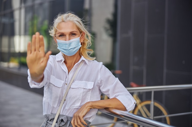 Close up of cheerful female in protective mask and white shirt looking and posing at the photo camera