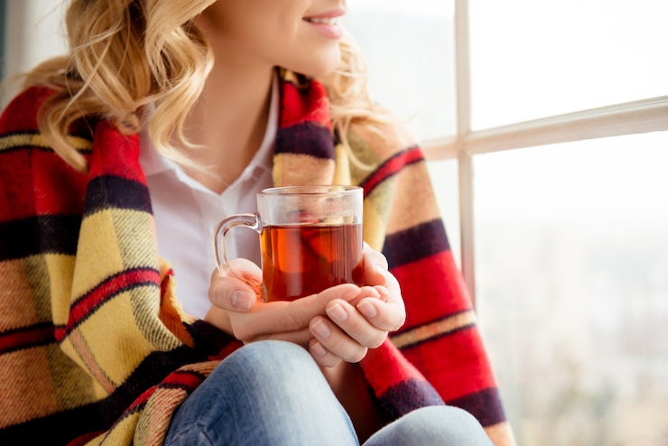 Photo close up on cheerful happy woman holding cup of tea and sitting on windowsill