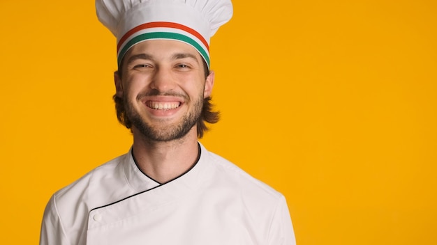 Close up cheerful male chef wearing uniform smiling at camera isolated on orange background Attractive bearded man in chef hat ready to cooking delicious food