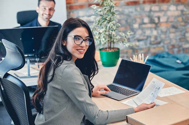 Close up of the cheerful pretty Caucasian woman in glasses laughing in the office room