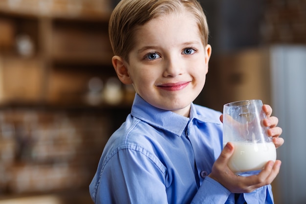 Крупным планом веселый улыбающийся маленький мальчик, выражающий радость, пьющий молоко