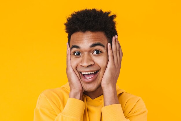 Close up of a cheerful young african teenager boy standing isolated on yellow