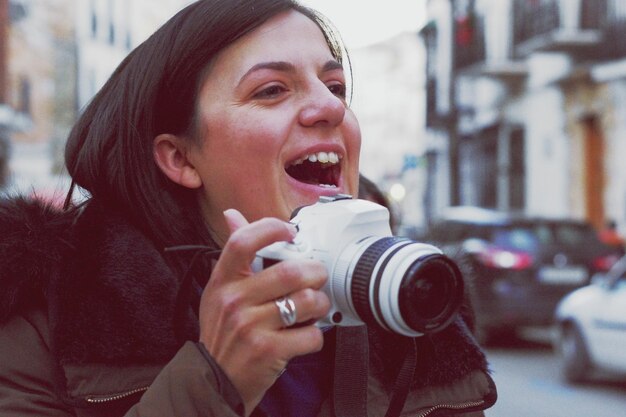 Foto close-up di una giovane donna allegra che tiene in mano la telecamera in città