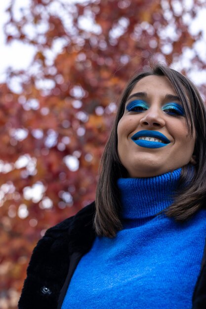 Close up of cheerful young woman with blue eye shadow makeup. Beauty portrait of female model with vivid makeup laughing on yellow background.