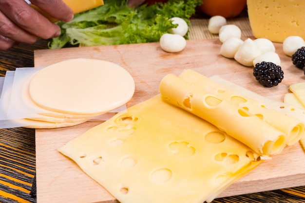 Foto chiusura del tagliere di formaggi con fette di formaggio svizzero e provolone e guarnito con frutta, servito su tavola in legno rustico con venature del legno