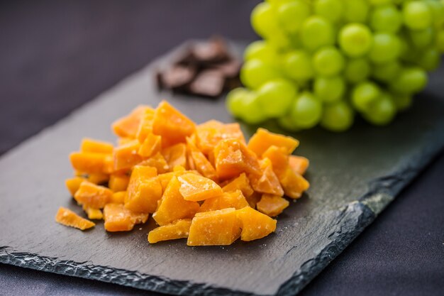 Close-up Cheese pieces and juicy grapes on slate board.