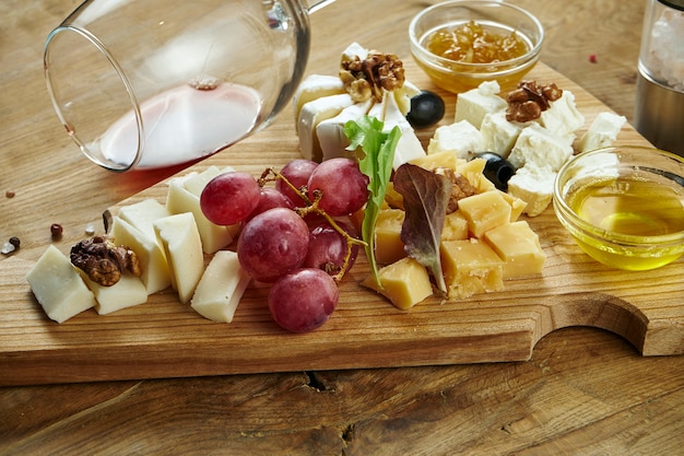 Close up on cheese plate served with nuts, grapes, honey. View from above on different types of cheese on dark surface