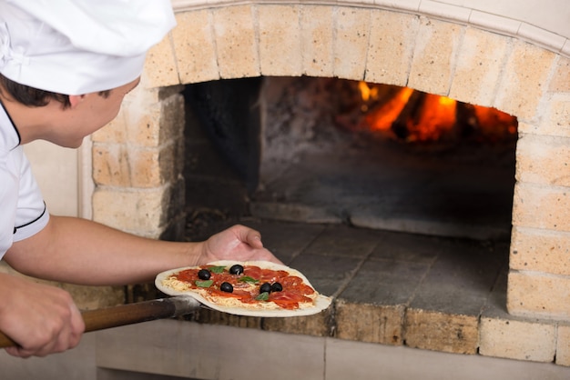 Close-up. Chef inserts a pizza in the oven.