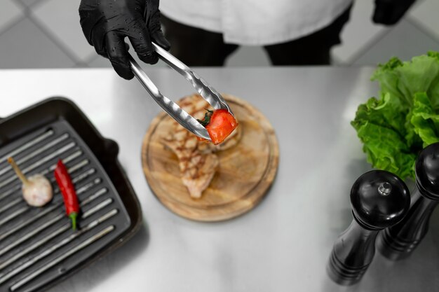 Primo piano della mano dello chef mentre mette un pomodoro dalla griglia su un piatto con le pinze