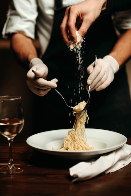 Primo piano della mano dello chef che versa il formaggio grattugiato sulla pasta