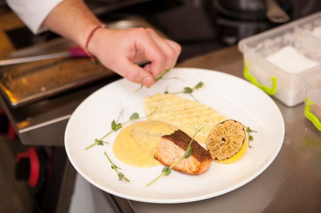 Close up of chefs hand adding greens to garnish delicious fried salmon