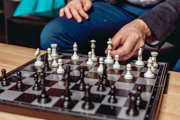 Close up chess board standing on the table. White and black figures. Male hand moving figures.