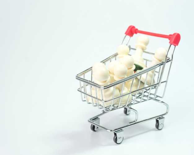 Close-up of chess pieces in shopping cart over white background