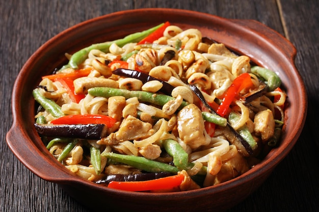 Close-up of chicken satay rice noodle with green beans, pepper and eggplant in a bowl on a wooden table, horizontal view from above