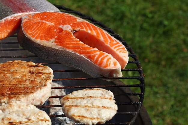 Primo piano hamburger di carne di pollo o tacchino per hamburger e bistecca di salmone preparata su una griglia per barbecue all'aperto, vista dall'alto