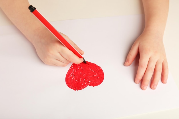 赤いハートを描く子供の手のクローズアップ