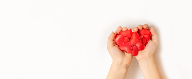 Close up of child hands holding red heart on white background