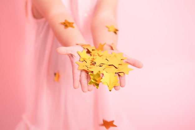 Close up of child hands with gold confetti kid in pink dress celebrating birthday