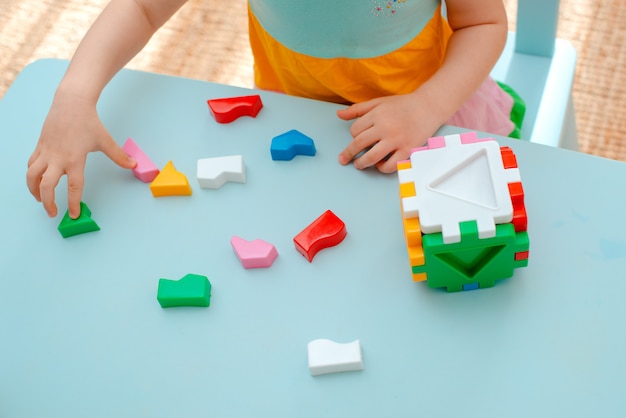 子供の手のクローズアップは、パズルの選別機を収集します。幾何学的形状と色付きのプラスチックブロックが挿入されたキューブ。