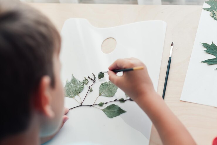 Photo close up of child sitting at desk and making picture from dry birch leaves autumn activities