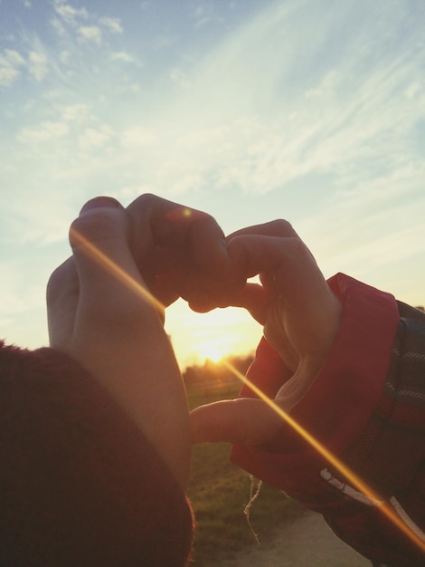 Близкий план детей, делающих форму сердца руками во время захода солнца