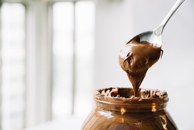 Photo close-up of chocolate spread on spoon over the glass jar