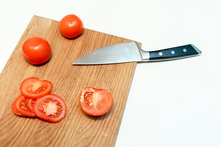 自宅のキッチンの木製まな板に刻んだ新鮮な完熟トマトとナイフのクローズアップ。