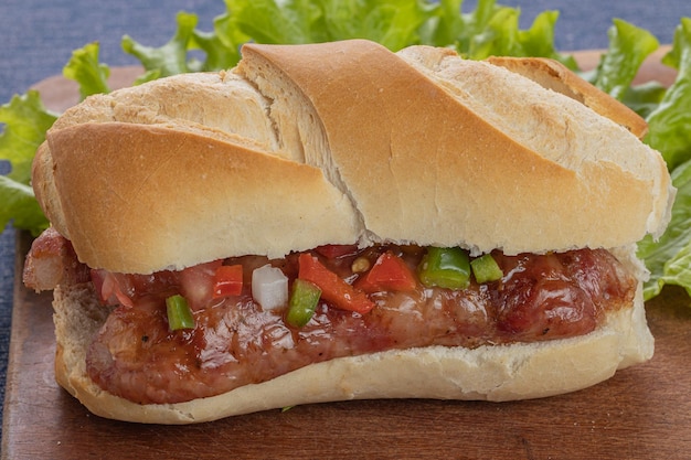 Close up of a choripan typical argentine sandwich with chorizo and creole sauce on a wooden board