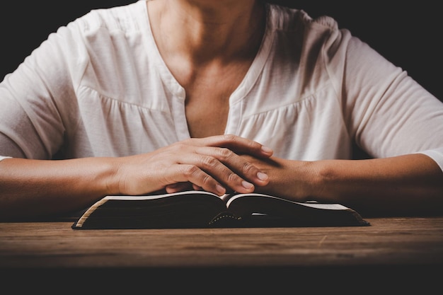 Close up of christian woman hand on holy bible are pray and\
worship for thank god in church with black background concept for\
faith spirituality and religion