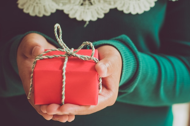 クローズアップクリスマスと新年の贈り物。女の子の手はクリスマスの赤いギフトボックス、手作りと工芸品を持っています。ヴィンテージスタイル。