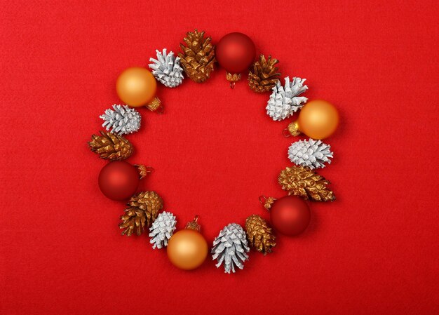 Close up Christmas wrath decoration of white and golden painted cones over red felt background with copy space, table top view, flat lay