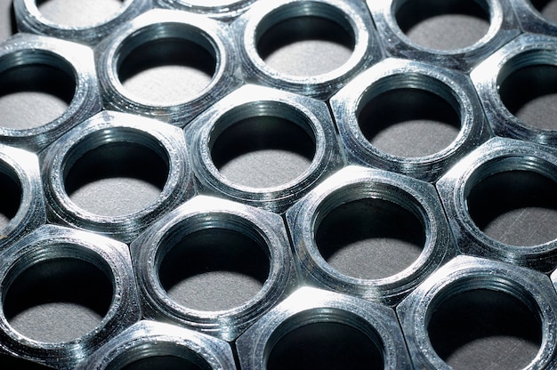 Close-up chrome metal nuts in the form of honeycombs lie next to each other forming an area