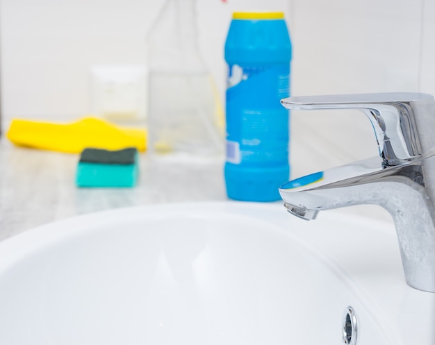 Close up of chrome sink spigot and cleaning chemicals, bottle, sponge and yellow rag with copy space