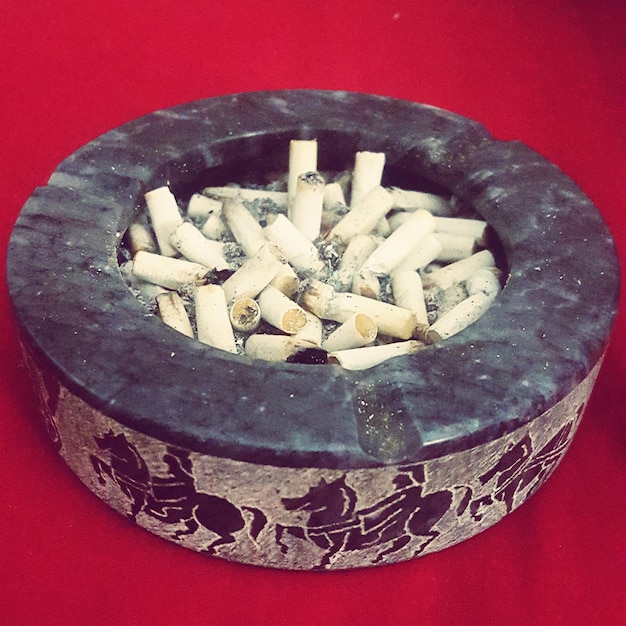 Photo close-up of cigarette butts in ashtray on red table