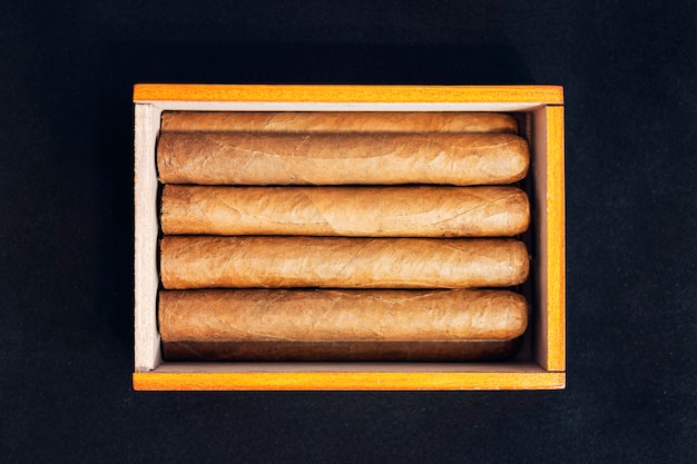 Close up of cigars in open humidor box on a black table in the dark.