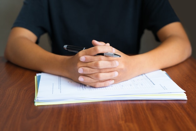 Close-up of clasped hands with pen on papers