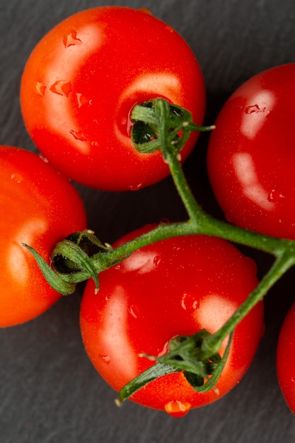 Close up of the clean ripe cherry tomatoes on the green branch having drops of water on them