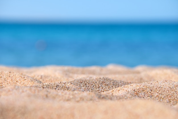 背景に青い海水で海辺のビーチを覆うきれいな黄色の砂の表面のクローズアップ。旅行と休暇のコンセプト。