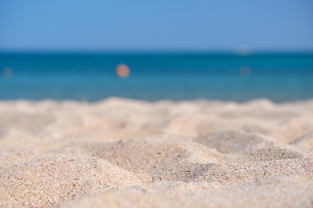 Close up of clean yellow sand surface covering seaside beach with blue sea water on background. Travel and vacations concept.